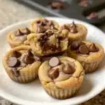 Stack of Reese’s Peanut Butter Chocolate Chip Cookie Bites on a rustic wooden table, showing melted chocolate chips and peanut butter cups inside.